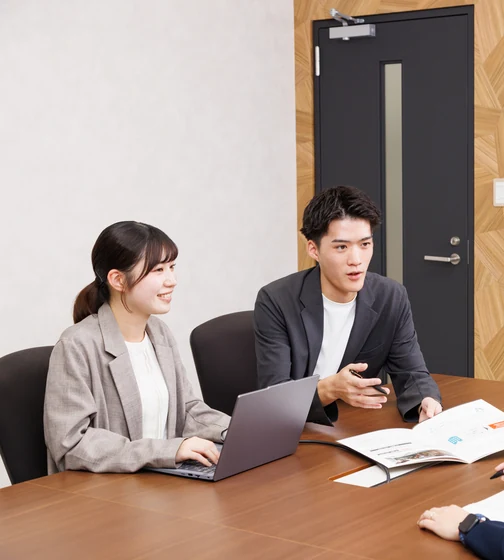 会議室で資料を見ながら打ち合わせる社員2名